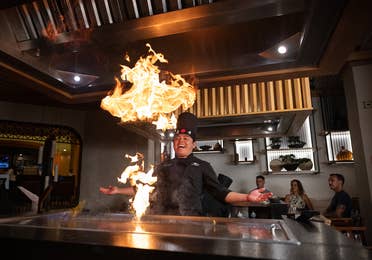 Man cooking on a hibachi grill with flames at Kinoko at Royal Haciendas Resort in Mexico.