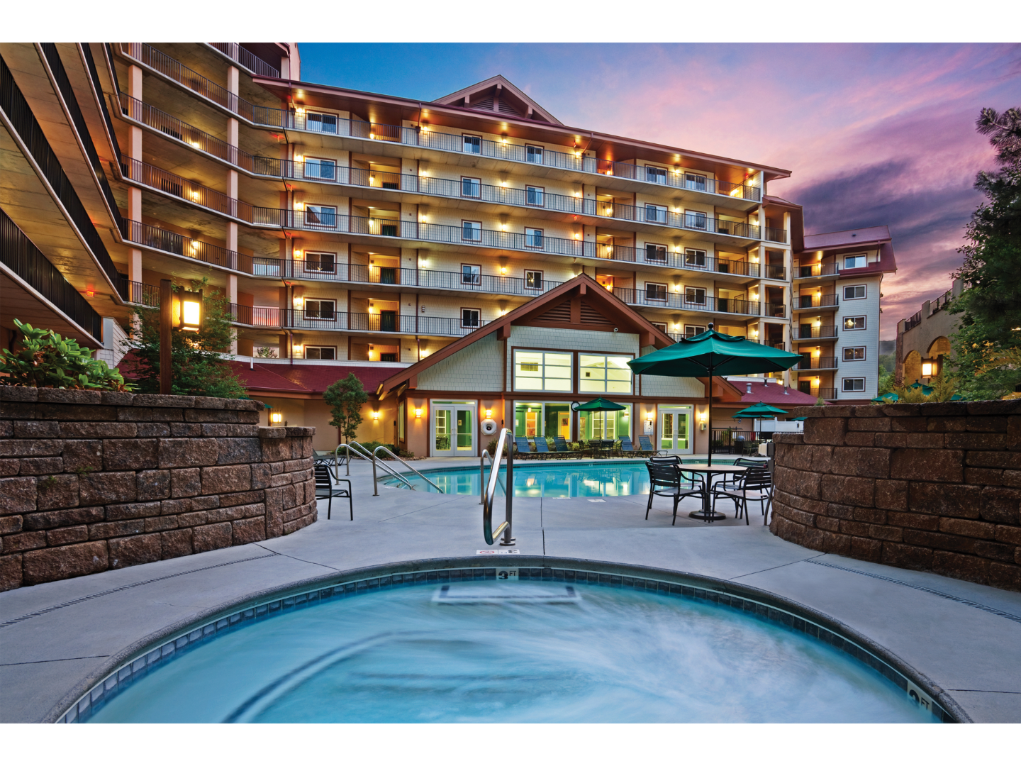 Resort building with balconies, pool, and hot tub at sunset, outdoor seating.