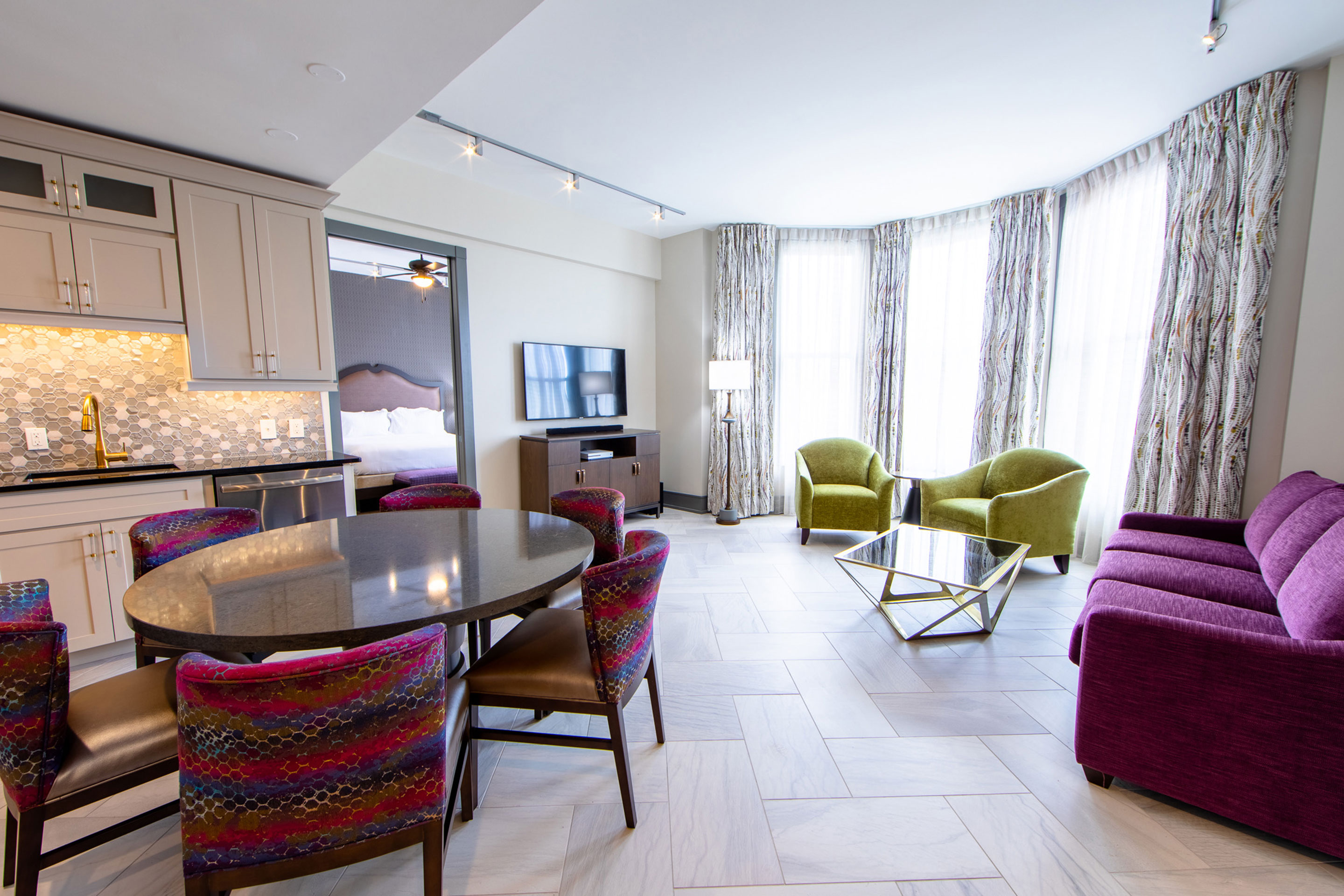 A kitchen with a round wood table and living room with green chairs, purple couch and a flat-screen tv in our Signature Collection villa in our resort in New Orleans, Louisiana.