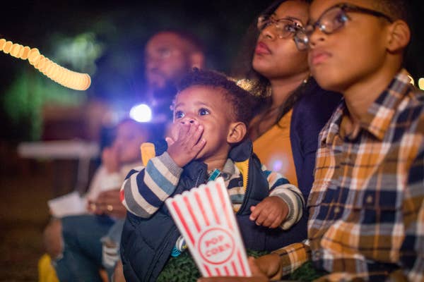 Toddler eating popcorn while watching a movie outside with his family