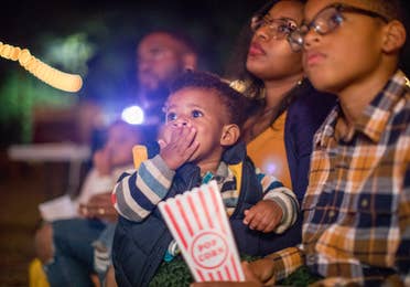 Toddler eating popcorn while watching a movie outside with his family