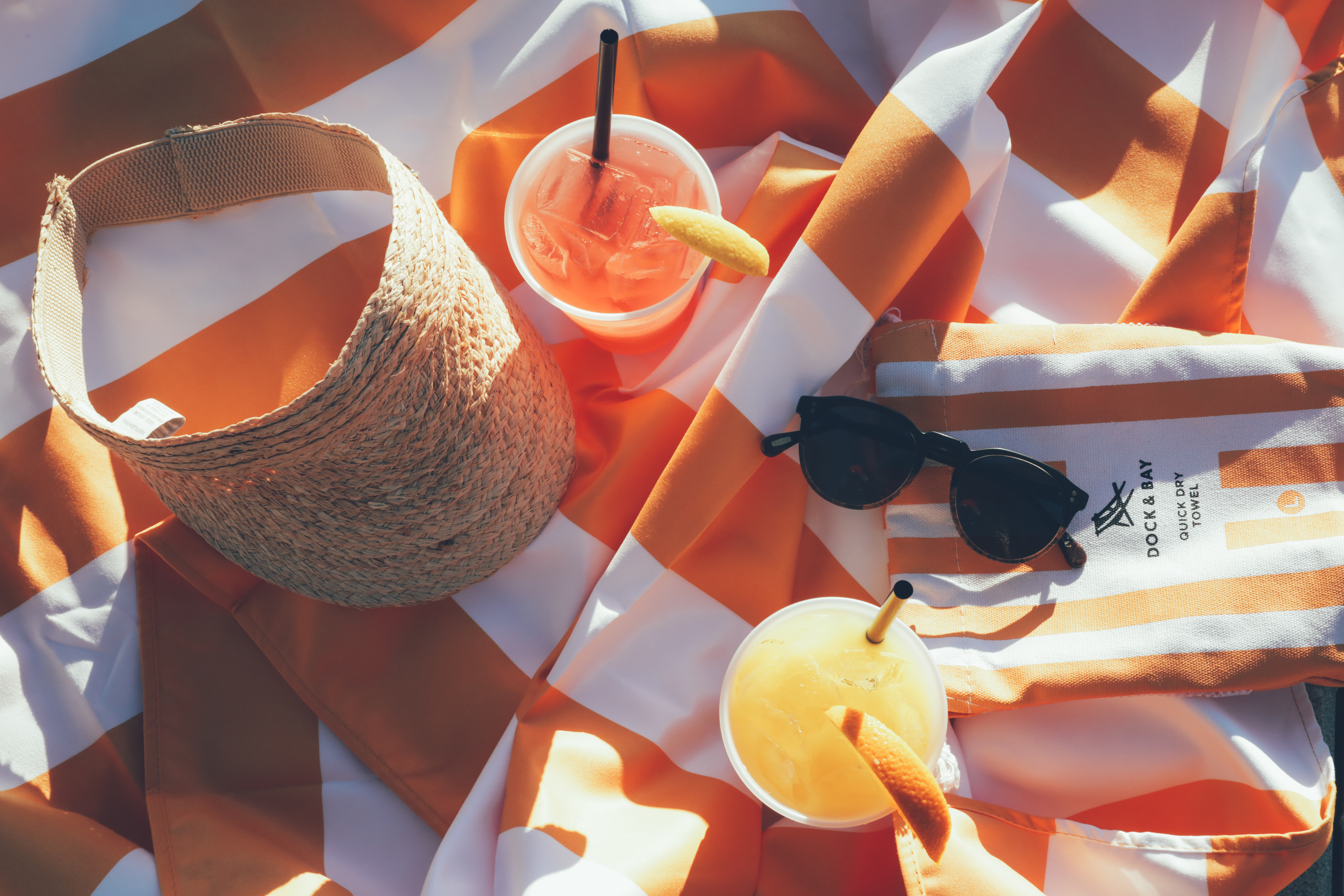 Fruity beverages, sunglasses, and a sun visor on an orange towel in West Village at Orange Lake Resort near Orlando, Florida