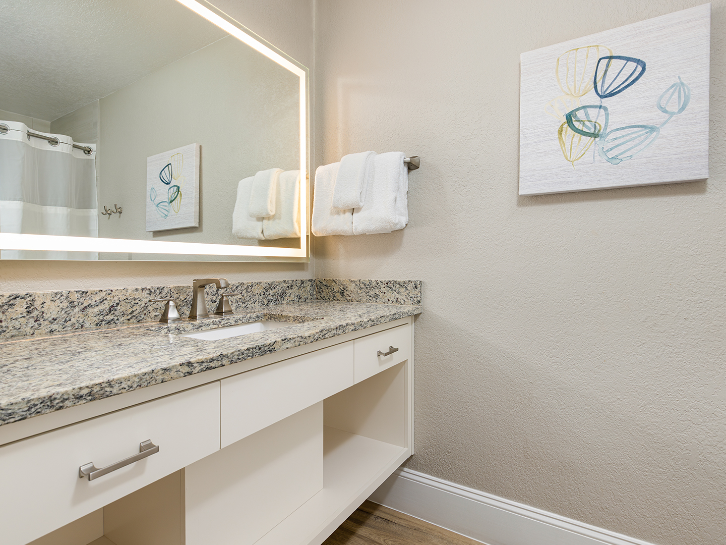 A bathroom vanity with a granite counter and illuminated mirror.