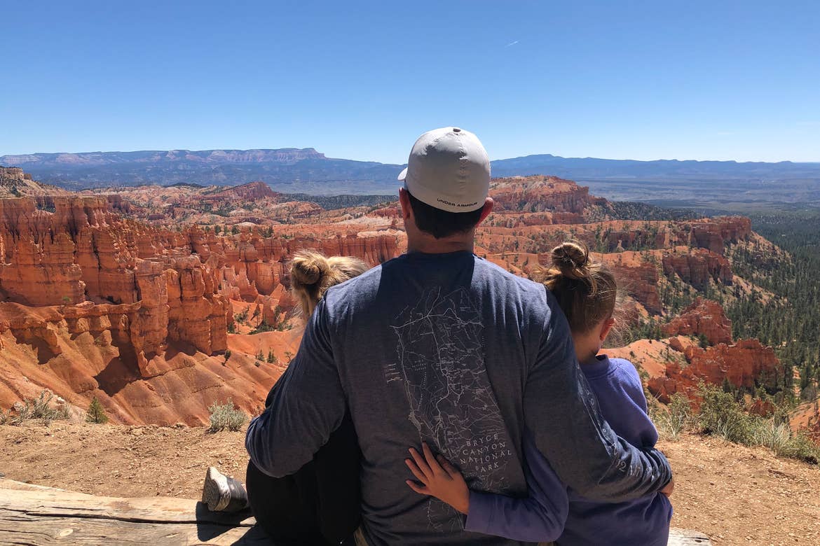 Chris' husband (middle) and daughters sitting at a Bryce Canyon National Park overlook.