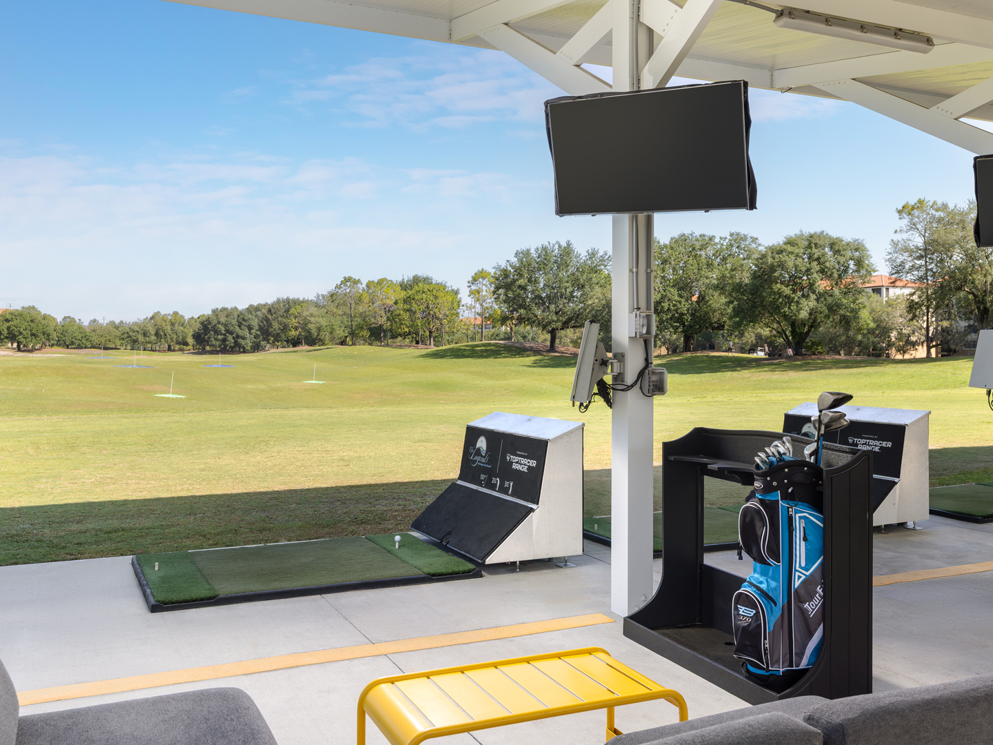 Driving range setup with golf clubs, monitor, and open green space.