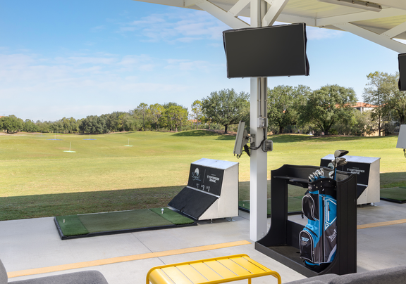 Driving range setup with golf clubs, monitor, and open green space.