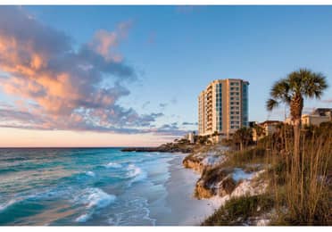 Clouds glowing pink float over rocky shoreline at sunset.
