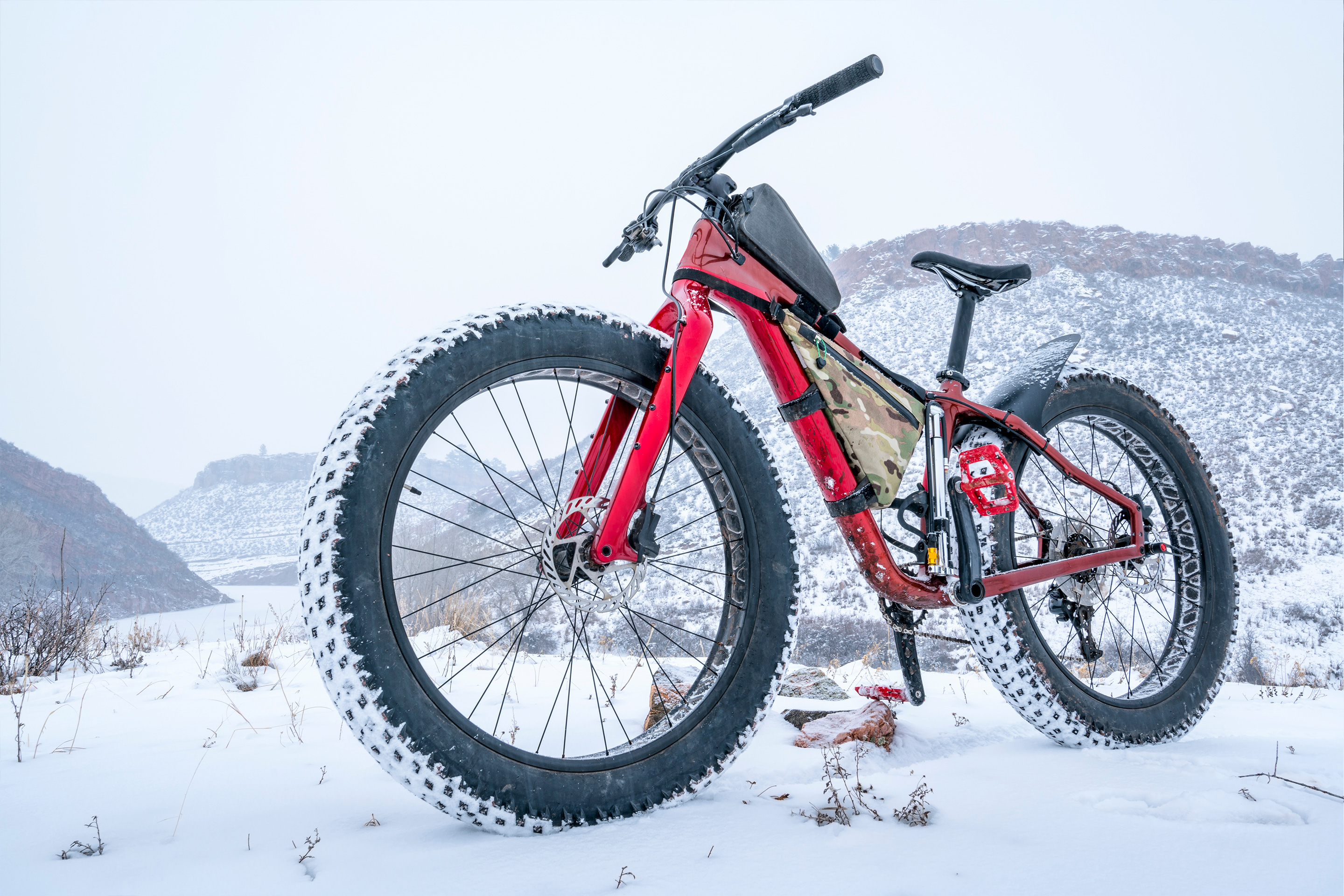 A red fat tire bike stands outdoors in front of a snowy mountain range.
