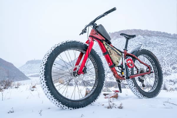 A red fat tire bike stands outdoors in front of a snowy mountain range.