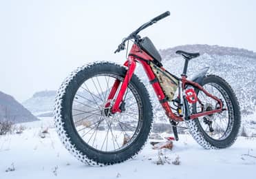 A red fat tire bike stands outdoors in front of a snowy mountain range.