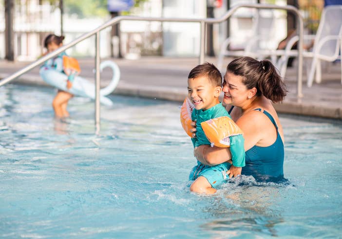 Adult holding child while laughing in resort pool at Holiday Hills Resort in Branson, Missouri.