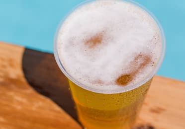 Cup of beer sitting out by a pool.