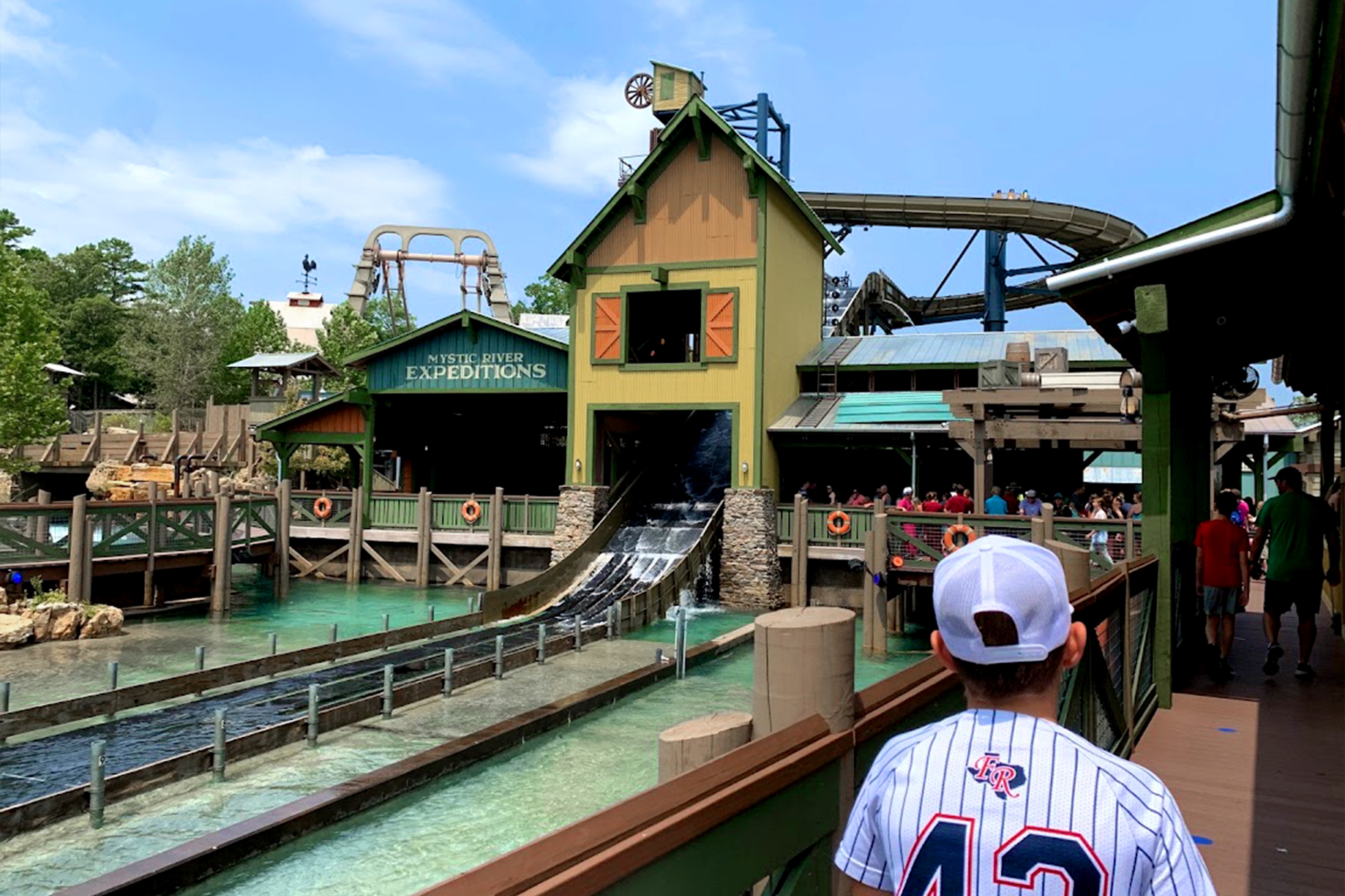 A water log ride with people waiting in a queue near a yellow, and multicolored wooden structure.
