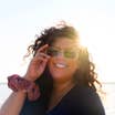 A woman wearing a black t-shirt and sunglasses in front of a sunset.