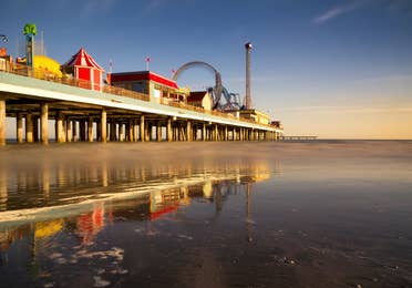 View of the Galveston Pleasure Pier at twilight showing a smooth ocean and carnival rides in motion