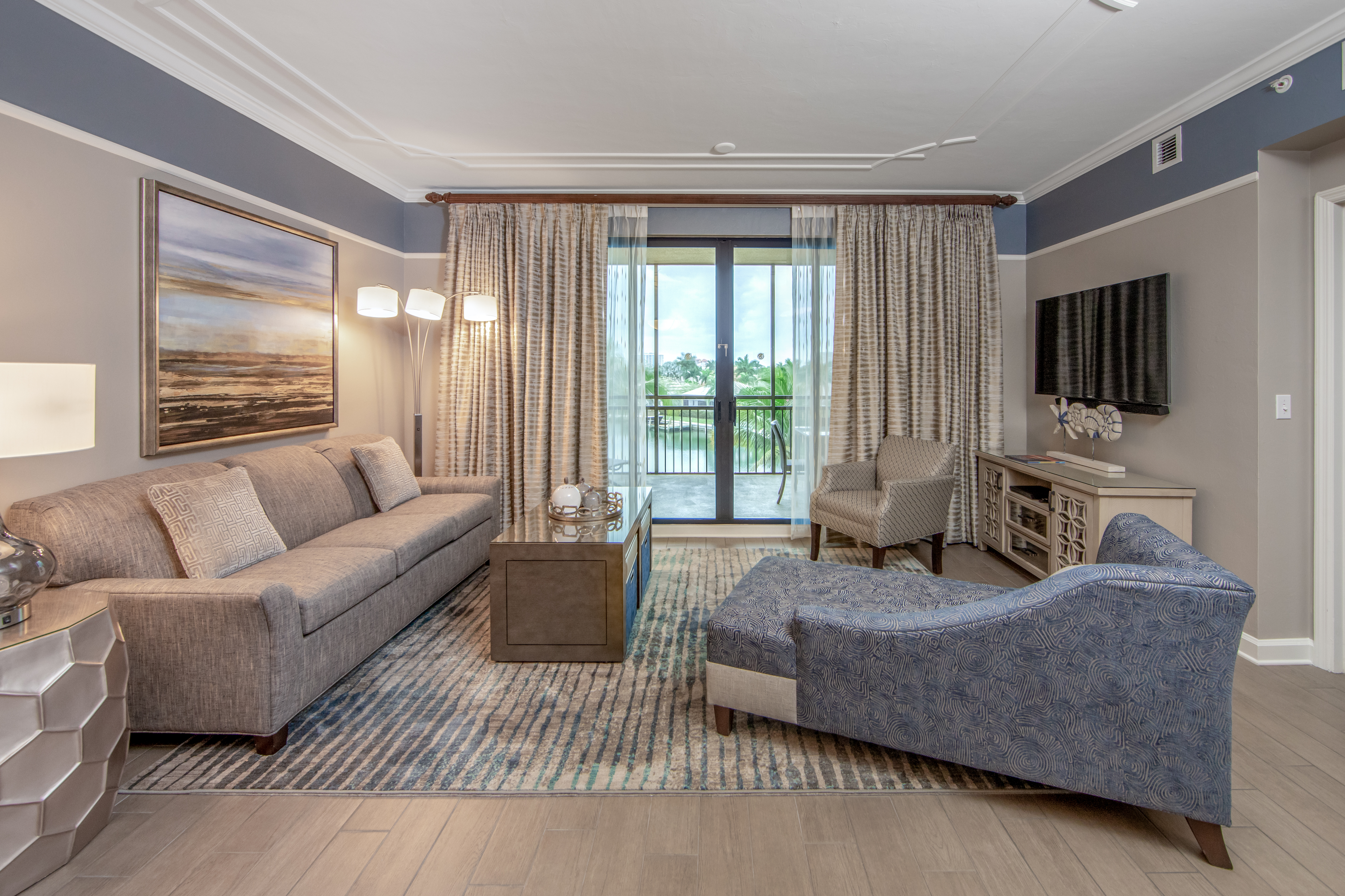 Living room with couch, two accent chairs, and flat screen TV with access to furnished balcony in a three-bedroom villa at Sunset Cove Resort in Marco Island, Florida