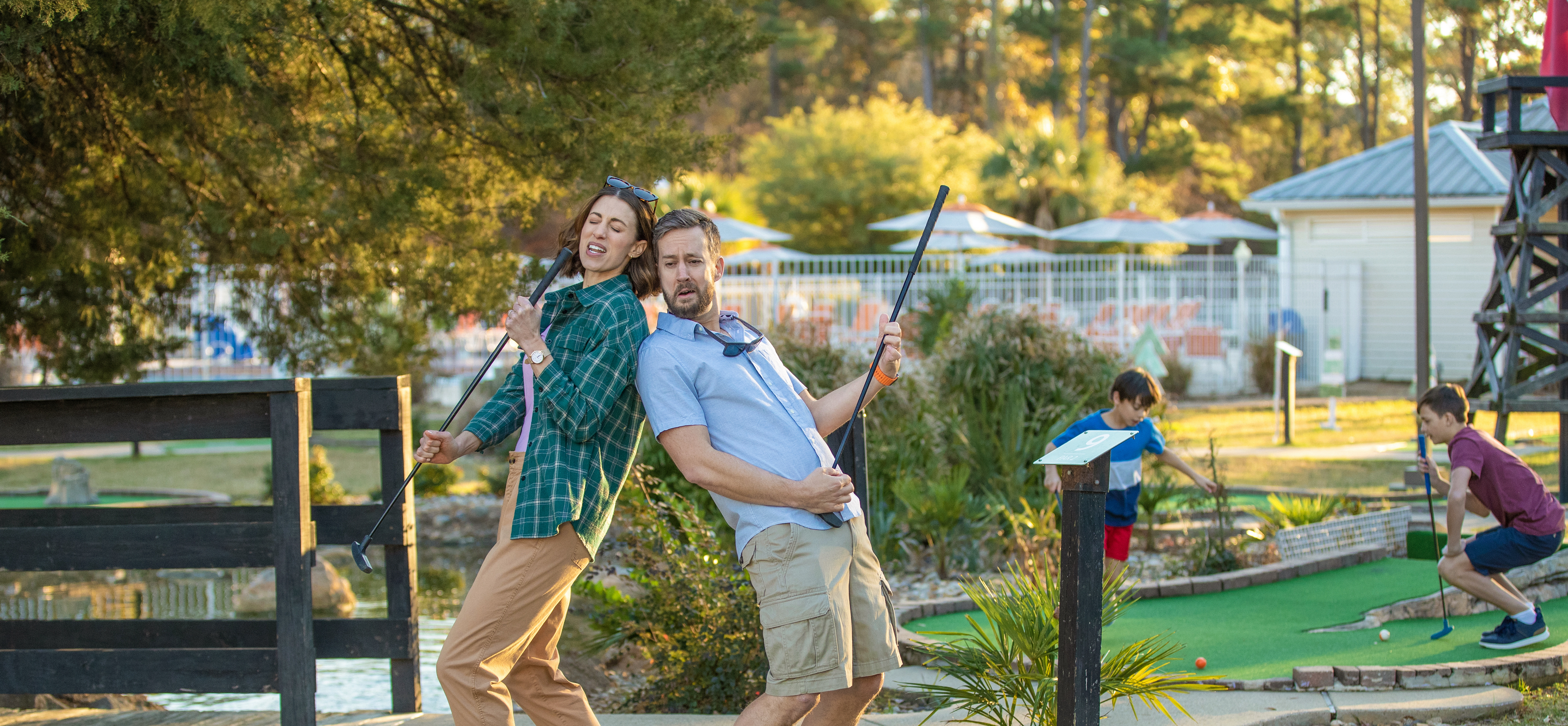 Man and woman on a miniature golf course and holding golf clubs like a guitar