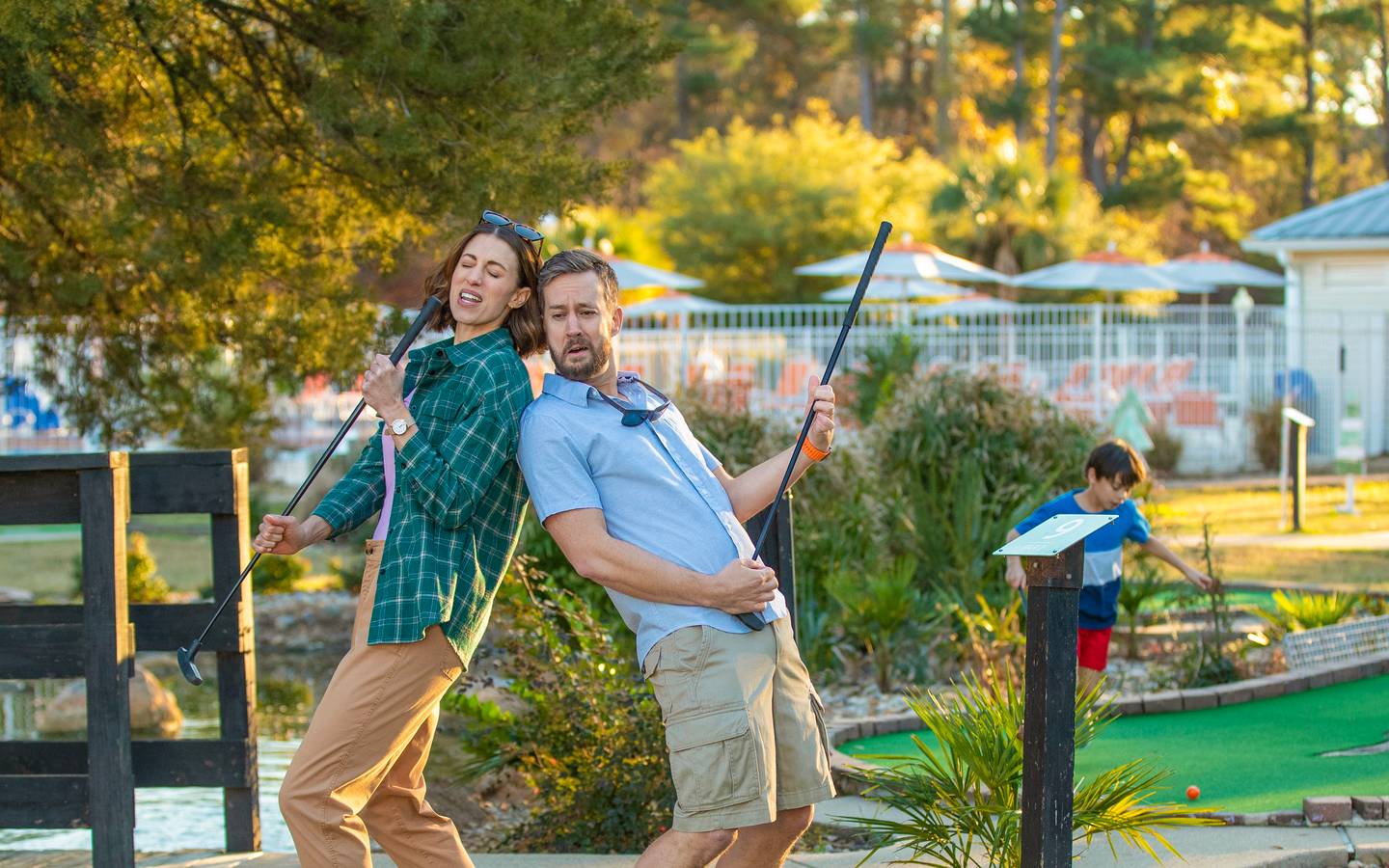 Man and woman on a miniature golf course and holding golf clubs like a guitar