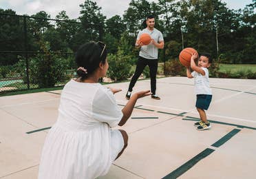 Family with two adults and small child playing basketball at Williamsburg Resort in Virginia.
