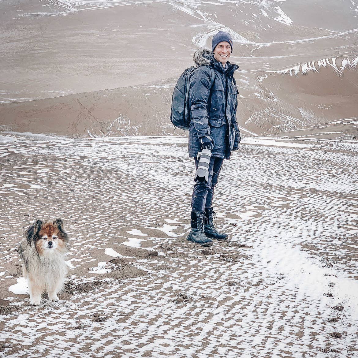 Author, Anthony LeDonne, stand in winter apparel with Bailey the Pomeranian at the Great Sand Dunes National Park and Preserve.