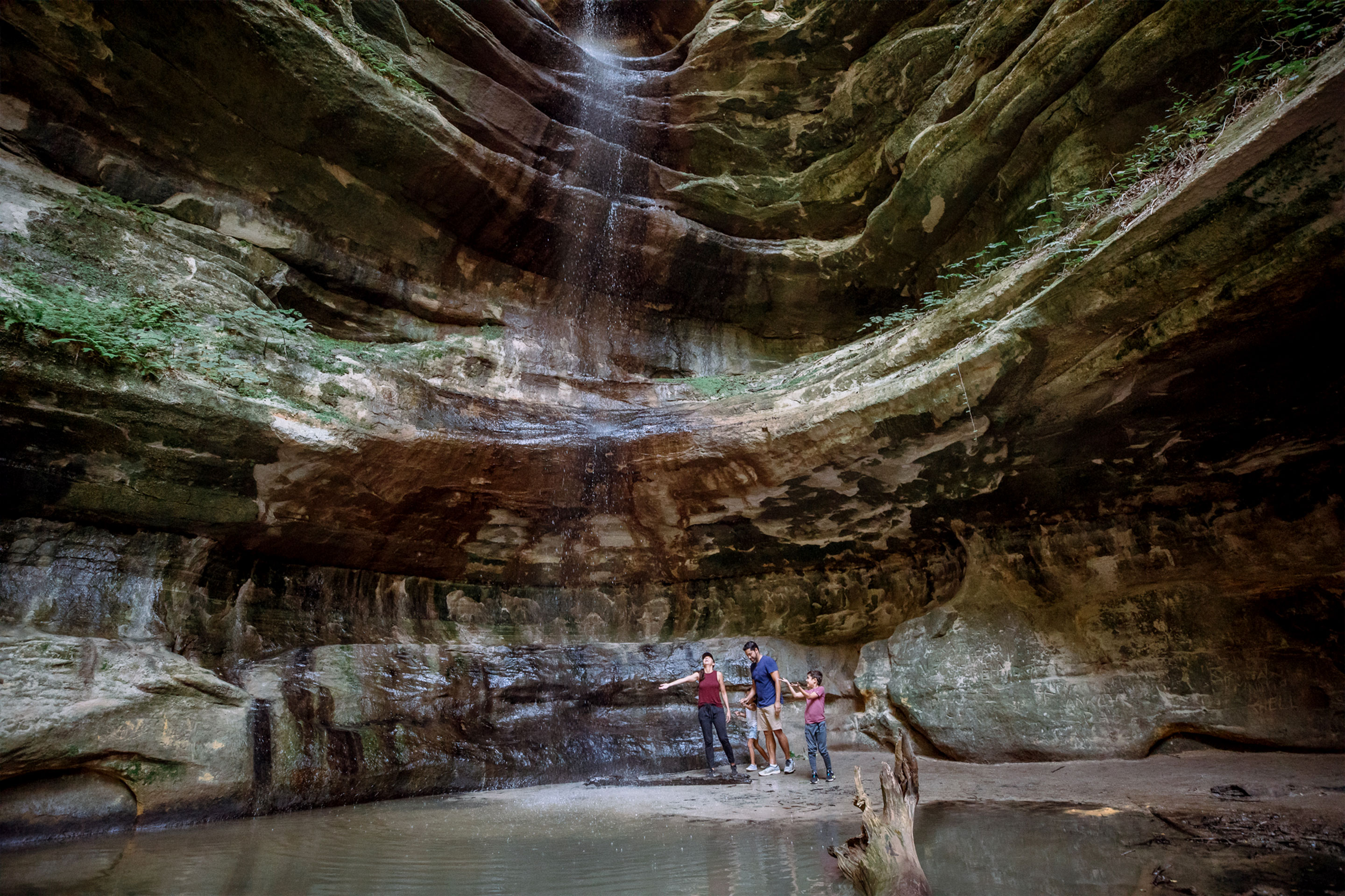 A woman, man, and two young children stand beneath a waterfall.