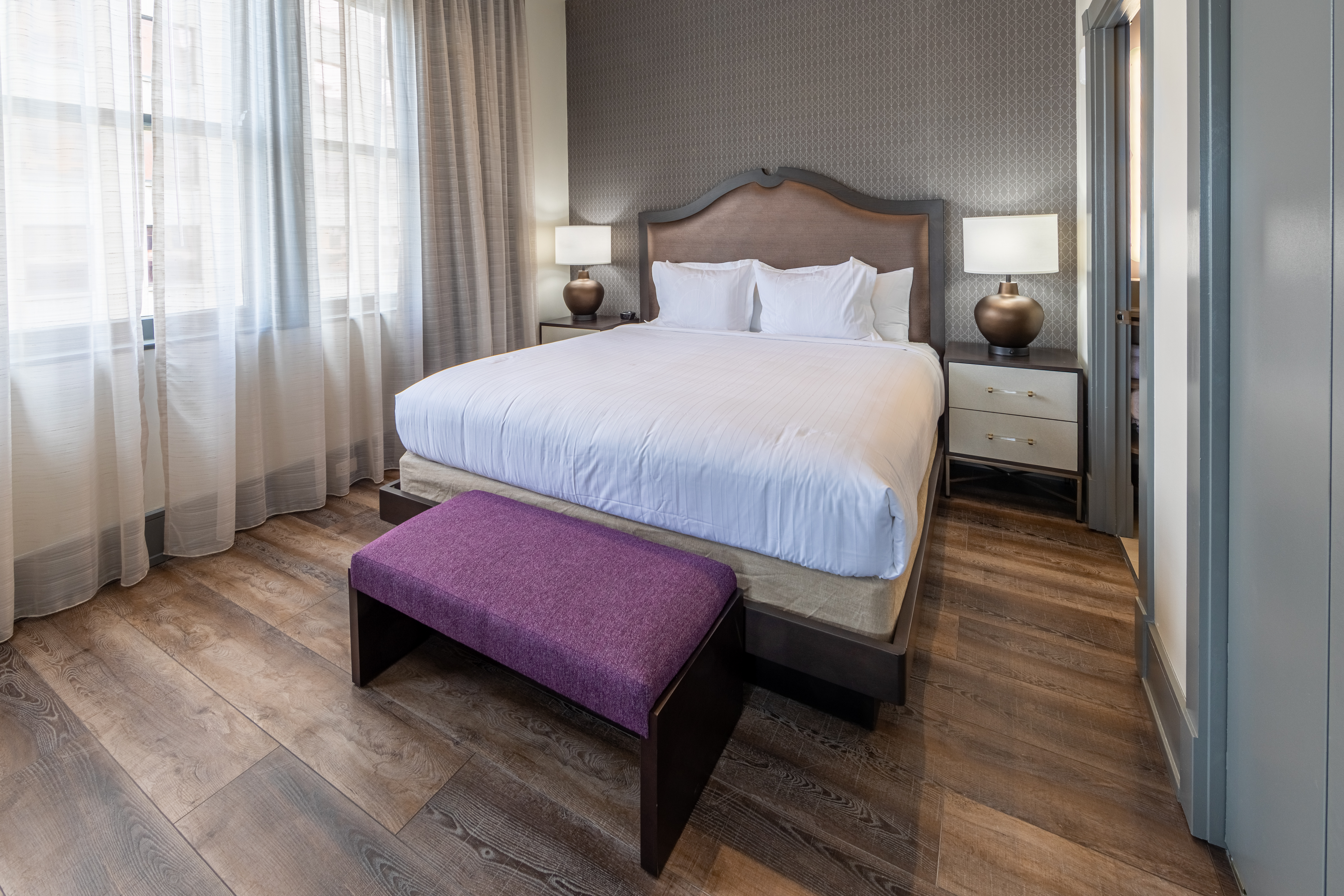 King bed with a purple bedroom bench and three windows in a one-bedroom Signature Collection villa at New Orleans Resort in Louisiana.