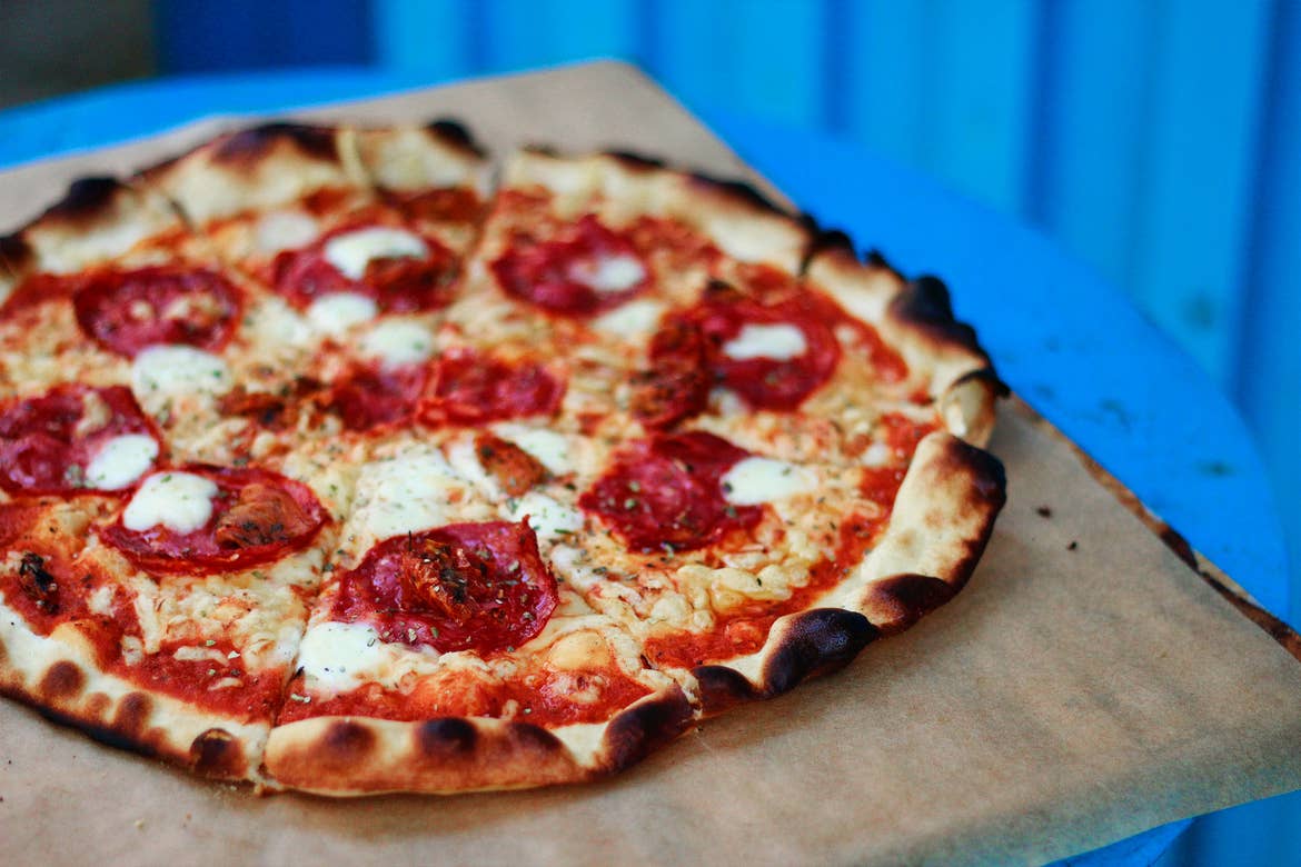 A pepperoni pizza placed on a wooden plank in a bright blue kitchen.