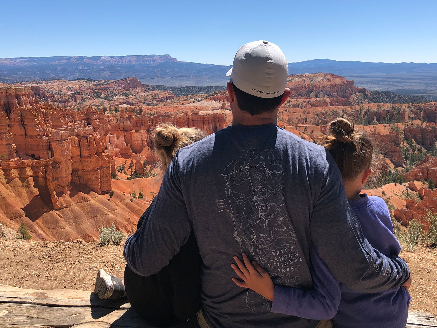 Chris' husband (middle) and daughters sitting at a Bryce Canyon National Park overlook.