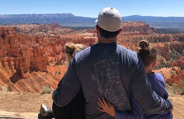 Chris' husband (middle) and daughters sitting at a Bryce Canyon National Park overlook.
