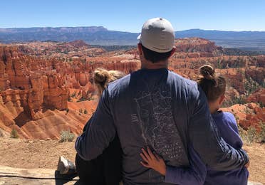 Chris' husband (middle) and daughters sitting at a Bryce Canyon National Park overlook.