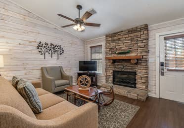 Living room with couch, accent chair, flat screen TV, and fireplace in a two bedroom cabin at Piney Shores Resort in Conroe, Texas