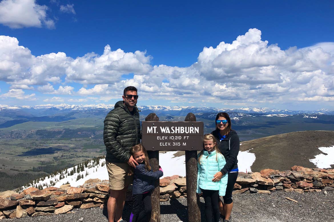 Author, Chris Johnston (far-right), stands in front of the Mt. Washburn elevation sign at Yellowstone National Park with her husband, Josh (far-left), and daughters, Kyndall (front-right), and Kyler (front-left).