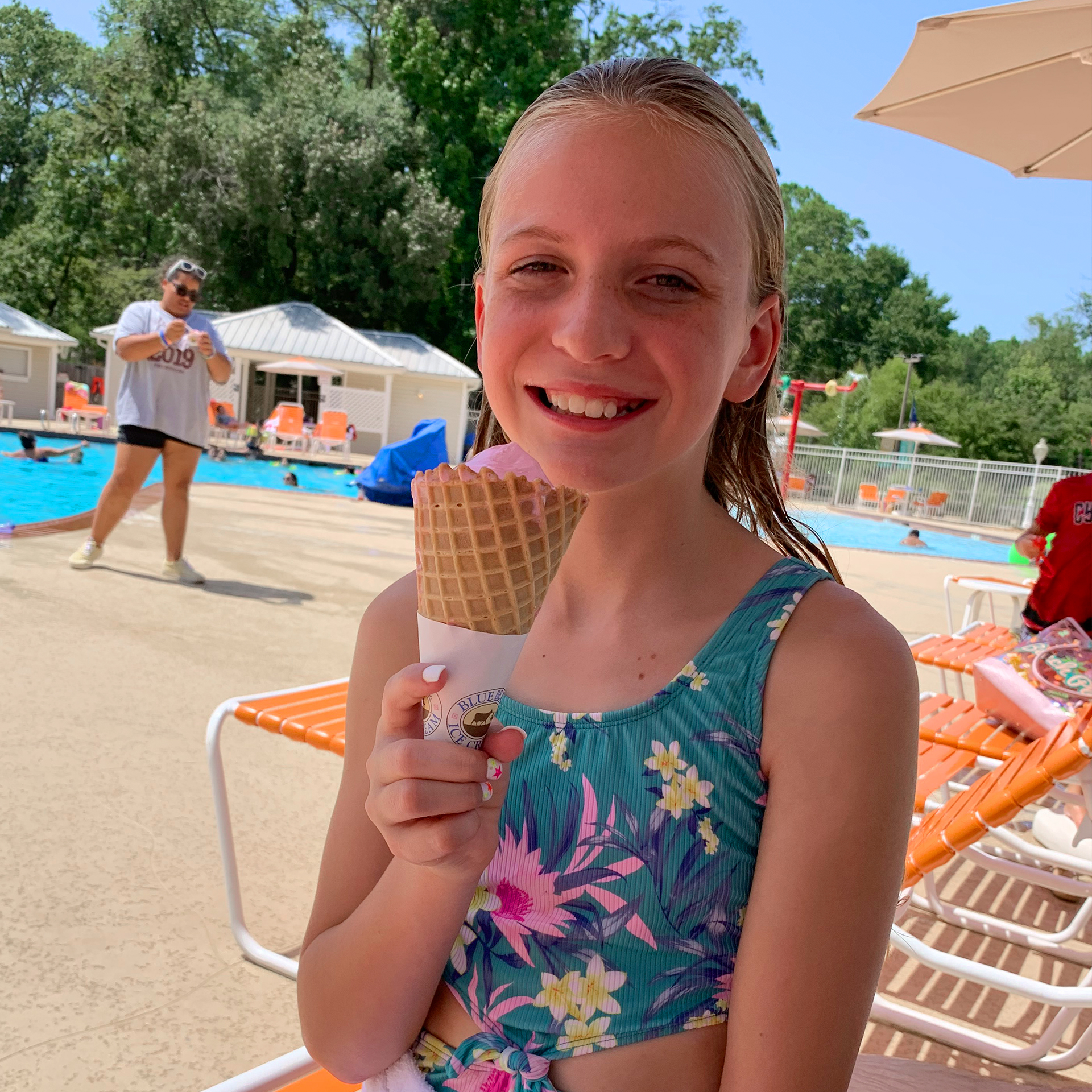 A caucasian girl eats an ice cream cone while wearing a swimsuit near a pool.