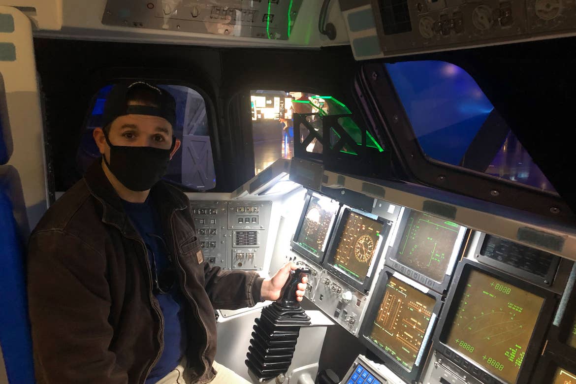 Featured contributor and Checking In Editor, Tori Ferrante's husband, Brooks wearing a mask in the cockpit of an Atlantis rocket simulator at the Kennedy Space Center in Cape Canaveral, Florida.