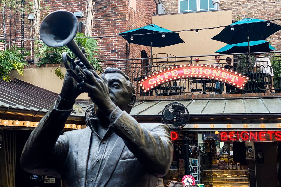 The exterior of Cafe Beignet sign and a bronze statue of a jazz performer.