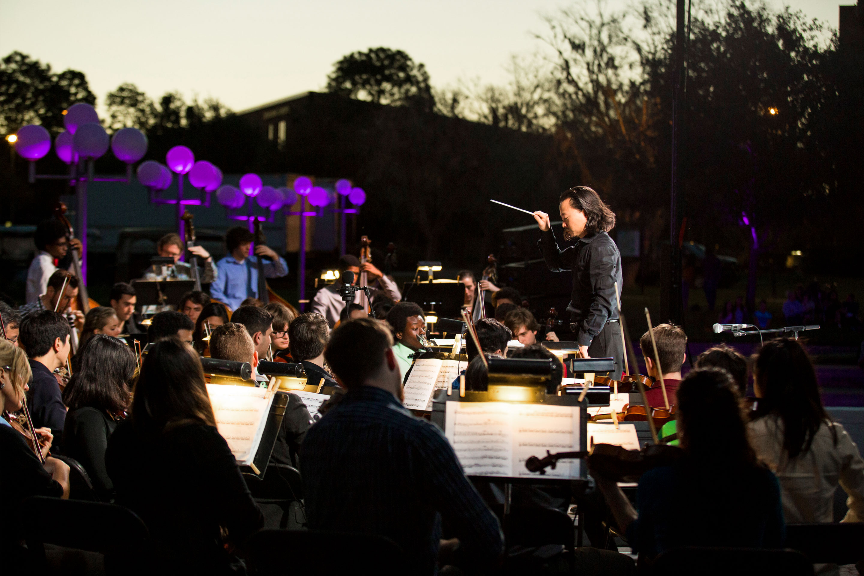 A man conducts a symphony orchestra outdoors.