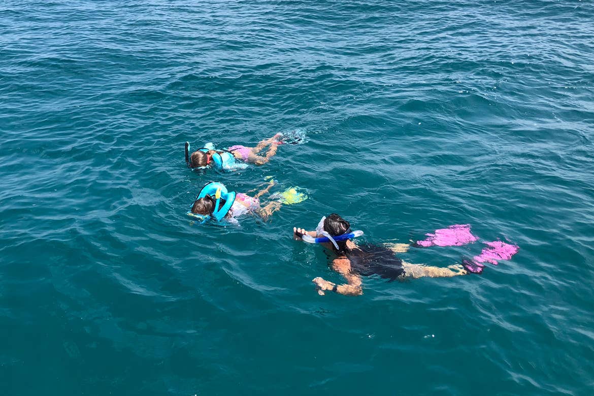 Featured Contributor, Chris Johnston (front-right),and her two daughters, Kyler (back) and Kyndall (middle), wear multi-colored snorkel gear while snorkeling in the ocean.