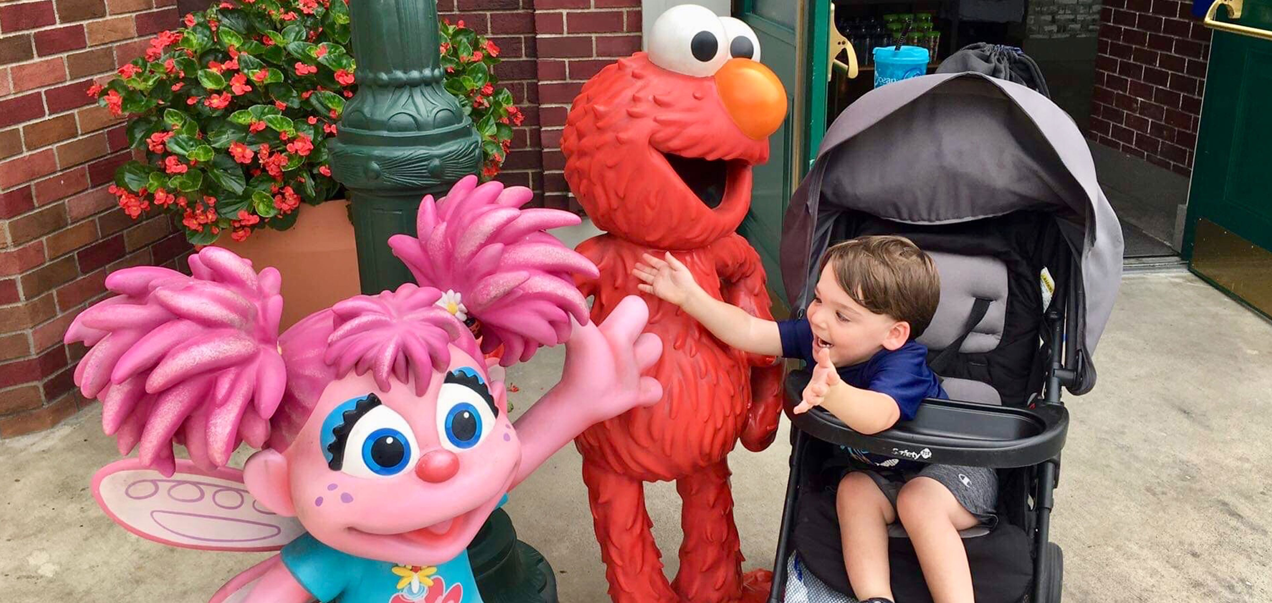 Dakota, Theresa's son, reaches from his stroller to embrace Elmo and Abby Cadabby outside Sesame Street Land.