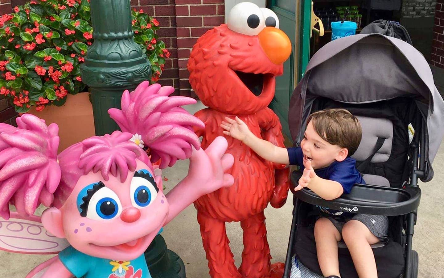 Dakota, Theresa's son, reaches from his stroller to embrace Elmo and Abby Cadabby outside Sesame Street Land.