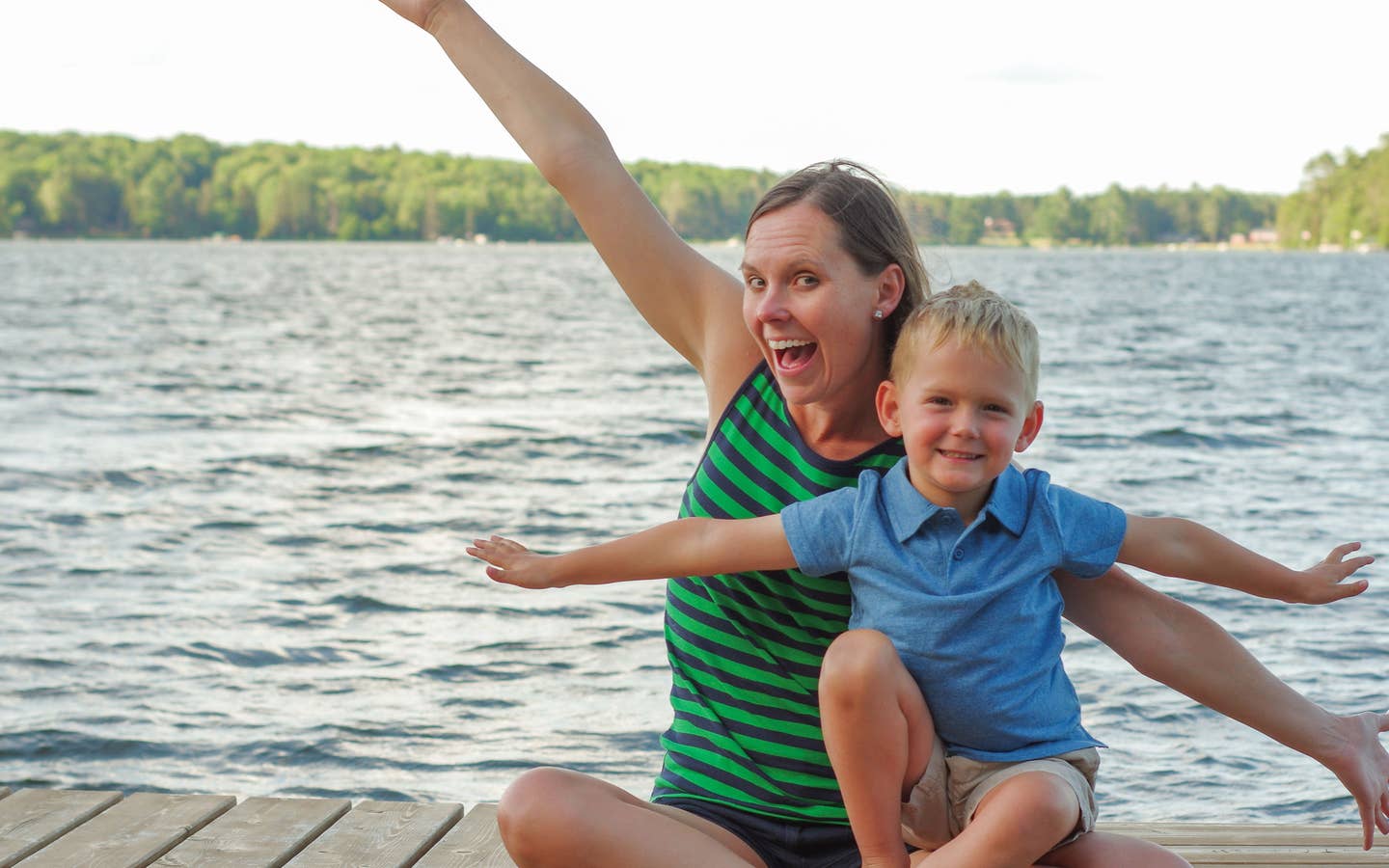 Author, Sarah Conroy, and son, Logan, sit on a lake pier mimicking an airplane with their arms.