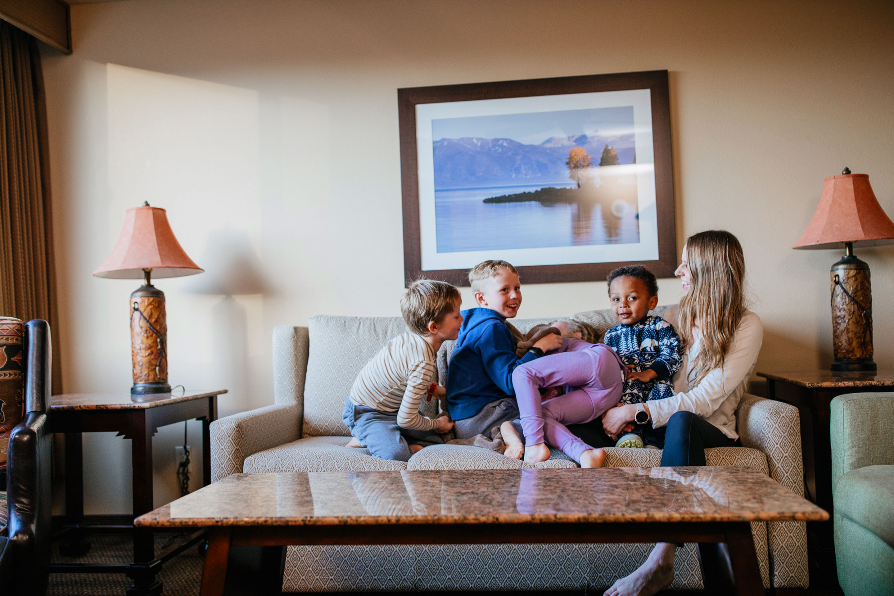 Four children in pajamas and a woman in jeans and a sweater cuddle on the couch.