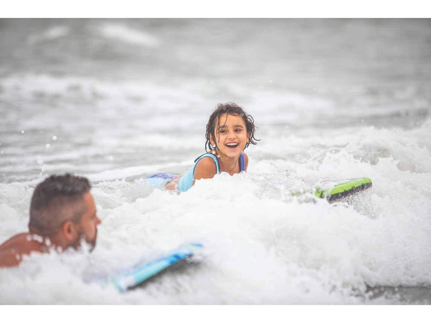 Smiling child rides a boogie board in ocean waves.
