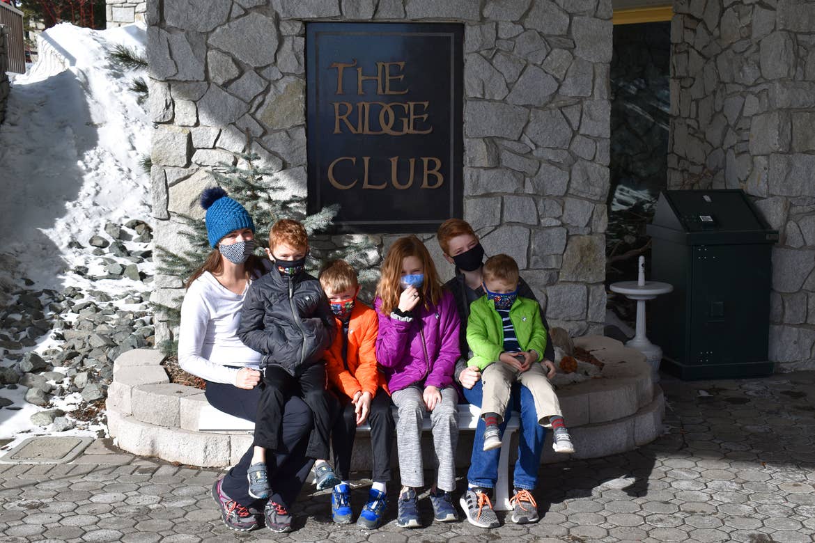 A woman and five children swear safety masks and winter apparel outside of a resort.