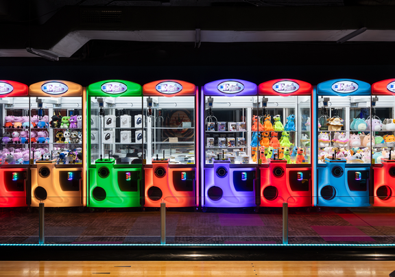 Colorful arcade claw machines lined up inside a game center.