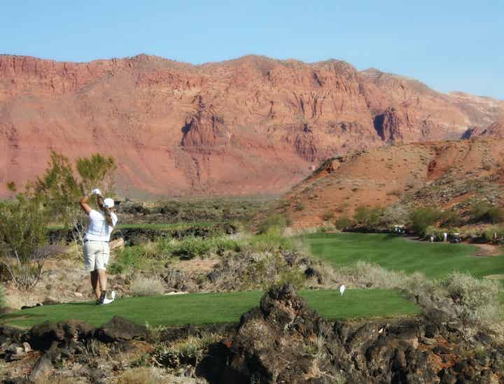 Person on a golf course and swinging a golf club with a desert mountain range in the background
