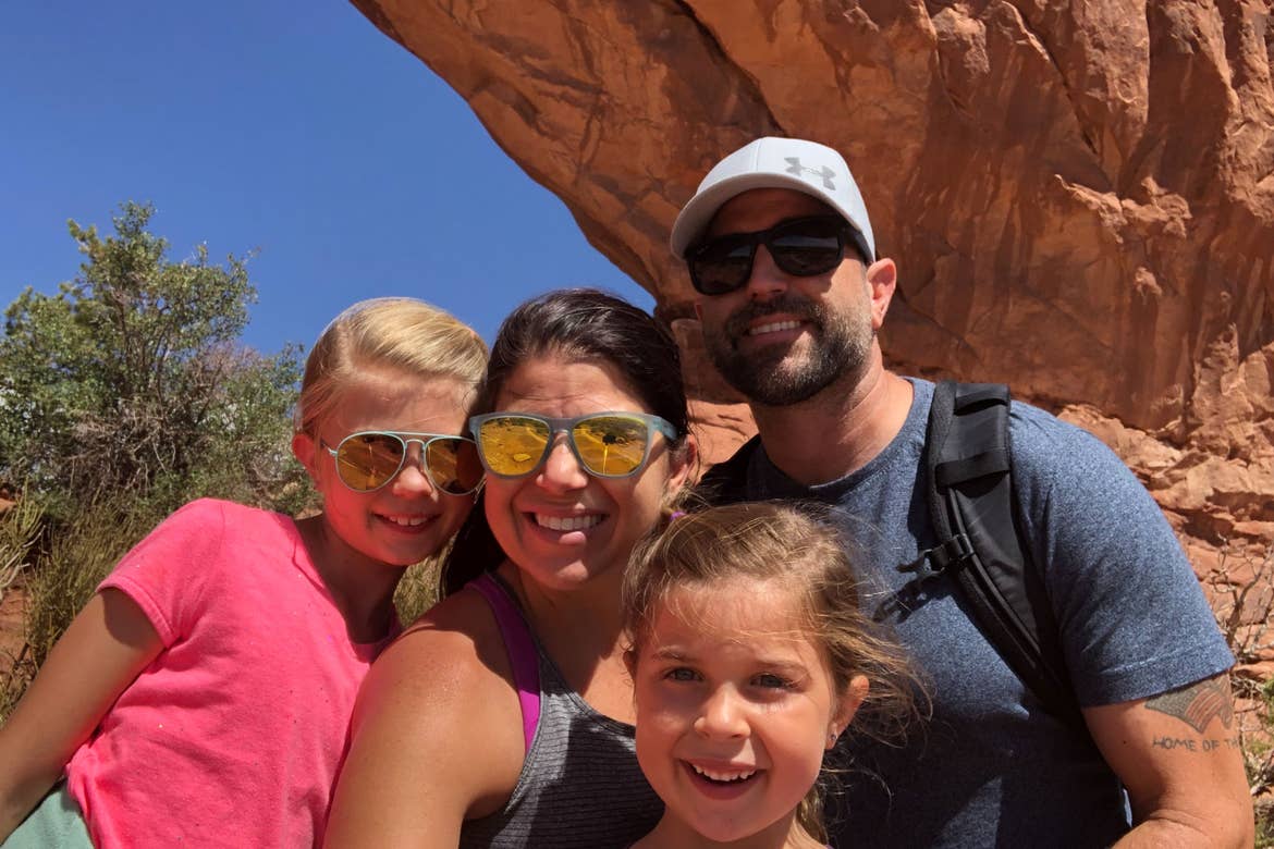 Chris (middle) with Josh (right) and daughters standing in front of the Delicate Arch Window Arch.