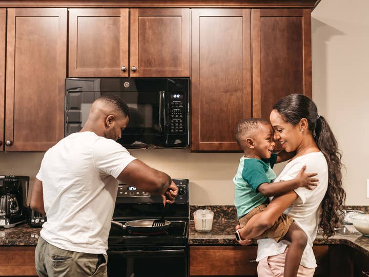 Woman holding a small child in their kitchen while a man prepares food on the stove at Williamsburg Resort in Virginia.