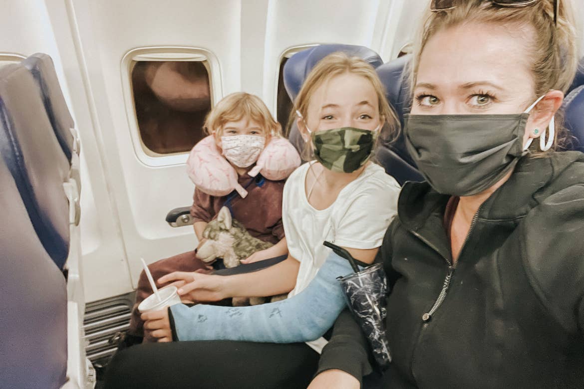 The Haby girls sit near a window seat while wearing masks on an airplane.