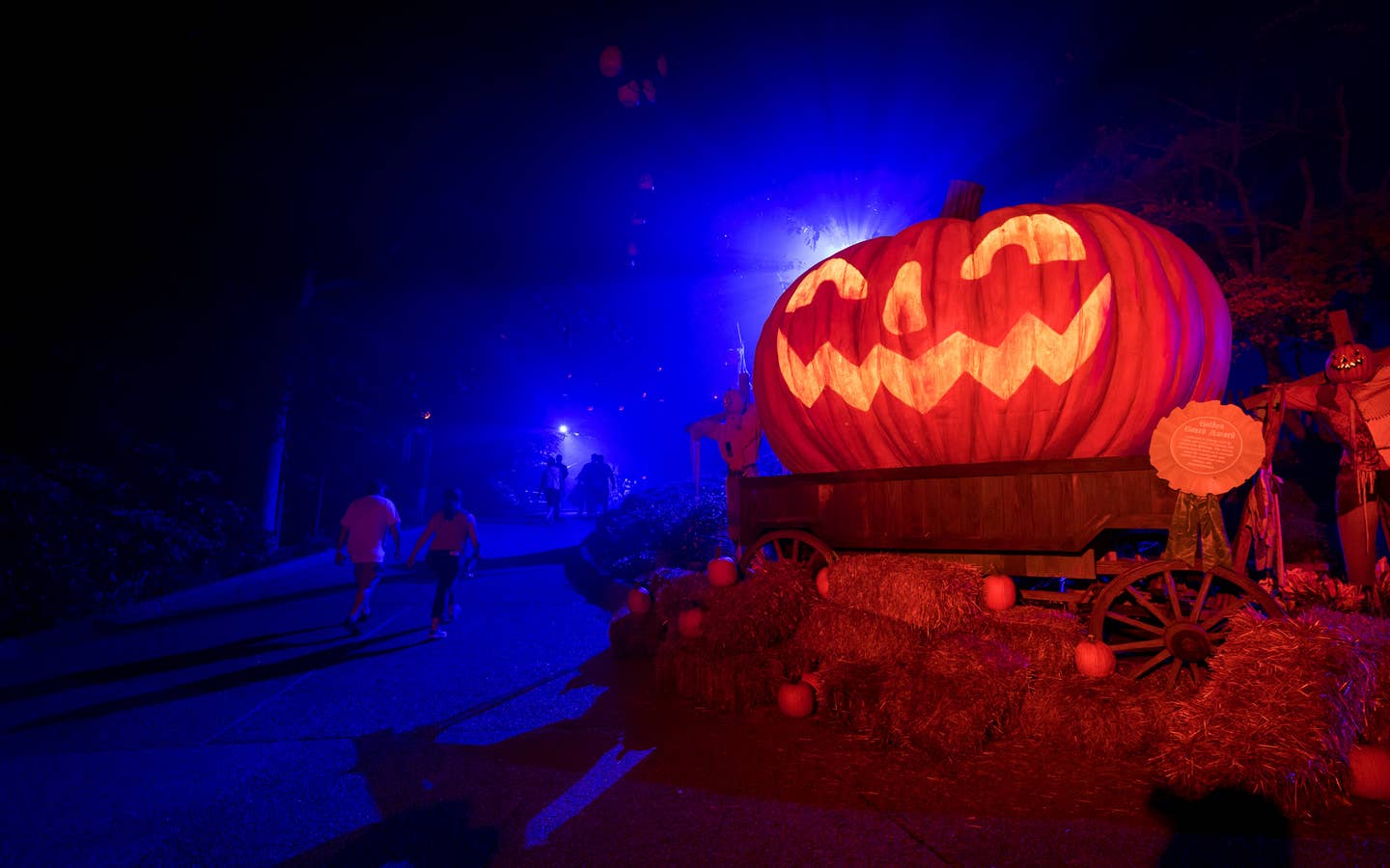 An oversized Jack O' Lantern sits on bales of hay at night.
