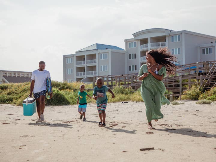 Family of four running onto beach from Galveston Seaside Resort in Texas.